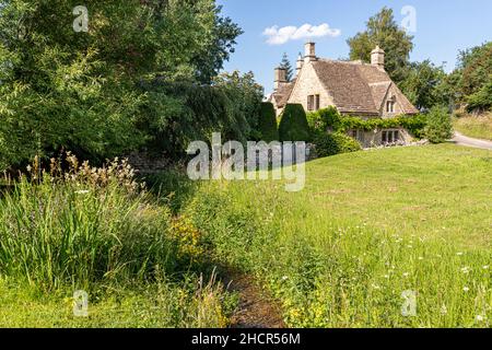 Un cottage tradizionale in pietra accanto al torrente nel villaggio Cotswold di Little Barrington, Gloucestershire Regno Unito Foto Stock