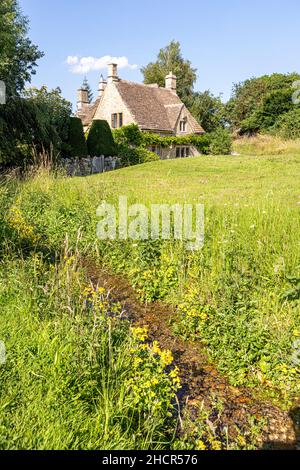 Un cottage tradizionale in pietra accanto al torrente nel villaggio Cotswold di Little Barrington, Gloucestershire Regno Unito Foto Stock