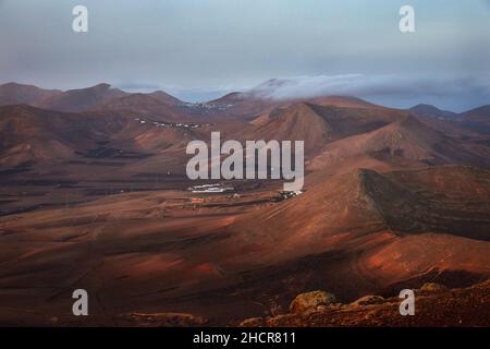 Alba a Lanzarote. Le nuvole di vento di commercio stanno venendo sopra le montagne e si dissolve. Vista al villaggio Femes e la catena montuosa Los Ajaches. Cana Foto Stock