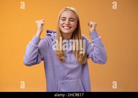 Trionfante festeggiamento positivo leale-capelli giovane femmina vincitore alzare mani clench pugni in su vittoria successo gesto chiudere occhi sorridendo ampiamente gla Foto Stock