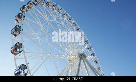 Frammento di un'attrazione ruota Ferris con cabina chiusa da vicino su uno sfondo blu cielo, vista dal basso. Ruota panoramica in una giornata di sole contro un blu Foto Stock