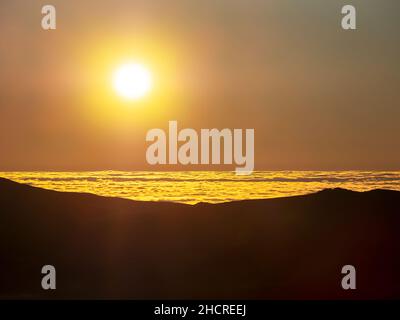 Guardando giù sul tramonto del sole sul mare irlandese dalle campane di Coniston con nebbia da un'inversione di temperatura, Lake District, Regno Unito. Foto Stock