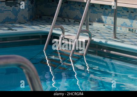 Dettaglio dei gradini e corrimano cromato della piscina esterna sulla linea di crociera Cunard Queen Elizabeth Foto Stock