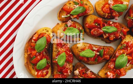 Stuzzicanti pomodoro antipasti italiani o bruschetta, su fette di pane abbrustolito baguette guarnita con basilico Foto Stock