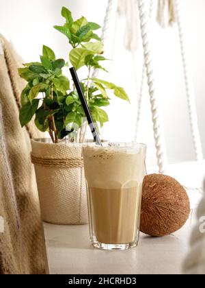 Latte di cocco in un alto bicchiere e cocco su un altalena in un caffè. Primo piano. Foto Stock