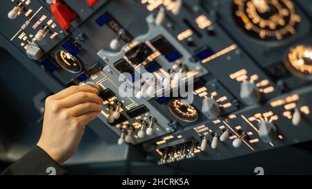 Primo piano della mano di un pilota che gira un interruttore a levetta sul pannello di controllo. Foto Stock