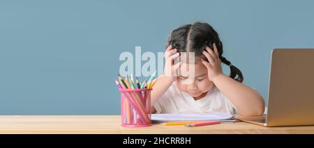 I bambini asiatici stanchi girl rimangono a casa e imparano da casa. La ragazza non motivata distracted dai compiti di lavoro della scuola, dai compiti, dal proble di istruzione dei bambini Foto Stock