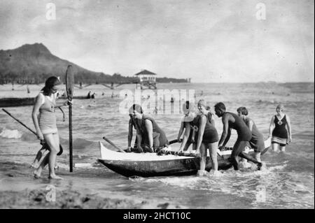 I salvatori di vita delle donne trasportano in canoa outrigger a Waikiki. Dopo la pratica nel surf questi membri del corpo salvavita delle donne tirano la loro barca sotto la direzione di David Kehanemoku, famoso uomo di canoa, 1920 Foto Stock