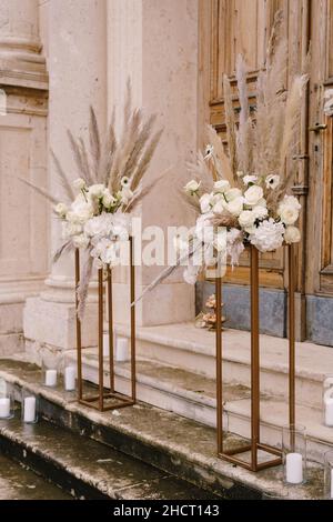 I mazzi di fiori si eriscono su plinti dorati sui gradini di fronte ad una porta di legno Foto Stock