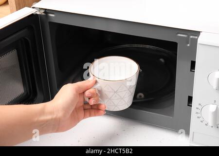Donna con una tazza d'acqua vicino al forno a microonde in cucina, primo piano Foto Stock