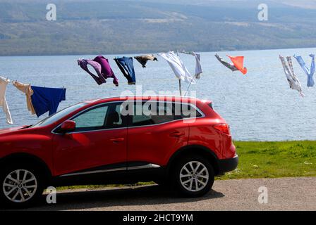 Auto rossa parcheggiata accanto a Loch Fyne, con il lavaggio domestico su linea di vestiti appeso all'asciutto, Inveraray, Argyll & Bute Foto Stock