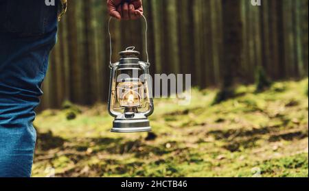 Escursionista che tiene una vecchia lampada a olio nella foresta. copyspace per il tuo testo individuale. Foto Stock