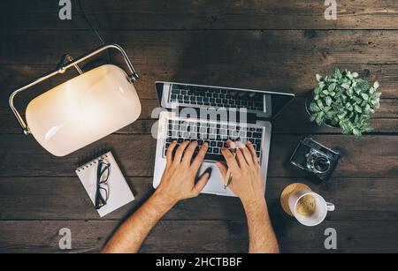 Vista dall'alto di un uomo d'affari che utilizza un notebook in ufficio a casa con lampada, tazza da caffè e fotocamera. Immagine del concetto di Vista dall'alto Foto Stock
