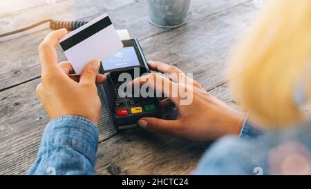 Primo piano della mano usando la macchina di swiping della carta di credito per pagare. Mano con carta di credito passare attraverso il terminale per il pagamento in caffetteria. Donna che entra credito Foto Stock