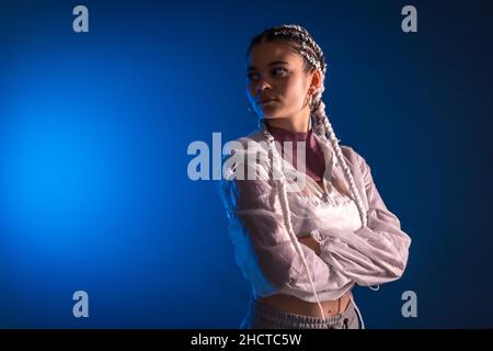 Sessione urbana. Giovane donna caucasica con lunghe trecce bianche su sfondo blu semplice, rap o trap danzer, copia spazio e pasta Foto Stock