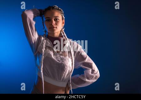 Sessione urbana. Giovane donna caucasica con lunghe trecce bianche su sfondo blu piano, rap o trap dancer, posa alternativa Foto Stock