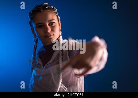 Sessione urbana. Giovane donna caucasica con lunghe trecce bianche su sfondo blu, rap o trap dancer Foto Stock