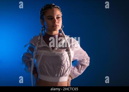 Sessione urbana. Giovane donna caucasica con lunghe trecce bianche su sfondo blu, rap o trap dancer Foto Stock