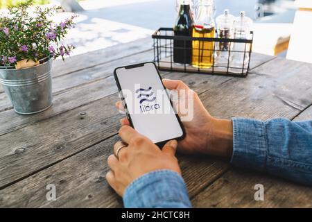 Donna che tiene in mano iphone X con il logo di Bilancia in un ristorante. Libra Facebook criptovaluta e criptovaluta bitcoin condivisione smartphone, Libra coin Foto Stock