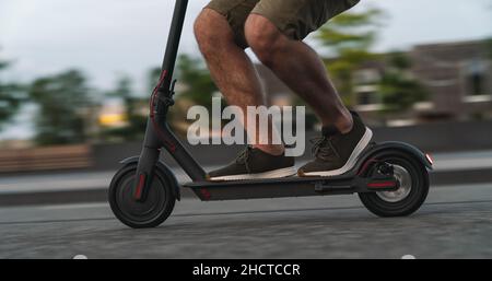 Primo piano di un uomo che guida il calciatore elettrico nero in città di notte con movimento sfocato Foto Stock