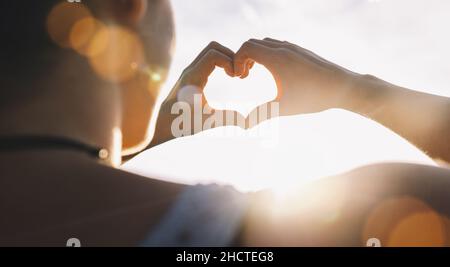 Mani femminili in forma di cuore contro il cielo passare raggi di sole. Mani in forma di amore cuore Foto Stock
