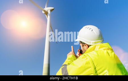 Il lavoratore di costruzione che ispeziona la turbina eolica, parlando con Walkie Talkie Foto Stock