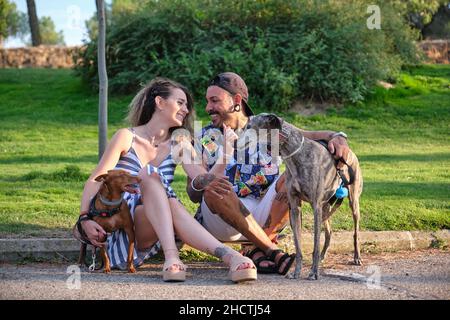 Giovane coppia tatuata abbracciata e seduta con i loro cani. Foto Stock
