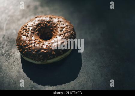 ciambella con glassato al cioccolato e spolverare su un tavolo scuro Foto Stock