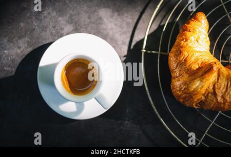 Croissant con espresso. Croissant francesi su griglia da forno e tazza di caffè espresso su sfondo di cemento scuro, vista dall'alto Foto Stock