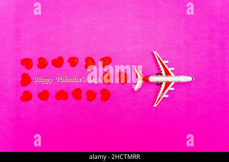 Giocattolo aereo e cuore su sfondo rosso, rosa, concetto di viaggio amore. Foto Stock