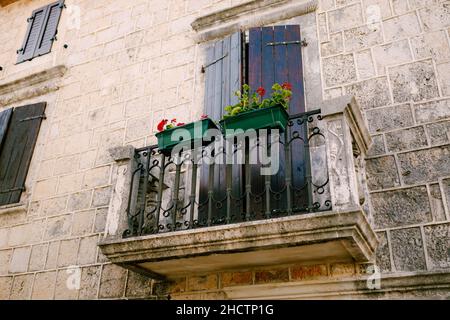 Balcone in pietra con traliccio in ferro battuto con vasi di fiori sulla facciata in pietra della casa Foto Stock