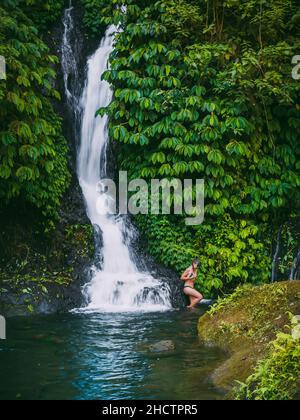 Cascata con donna in bikini e natura tropicale a Bali, Indonesia. Foto Stock
