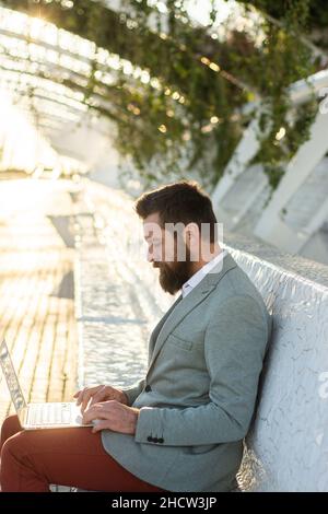 Bussinesman seduto e al lavoro guardando verso il basso un computer portatile che sta tenendo Foto Stock