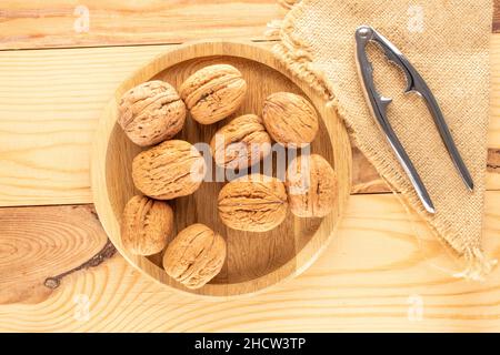 Diverse noci mature e deliziose con un vassoio di legno rotondo e un nutcracker in metallo su un tavolo di legno, primo piano, vista dall'alto. Foto Stock