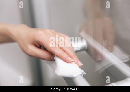 Pulizia delle maniglie delle porte in vetro con un panno antisettico umido. Donna mano che usa un asciugamano per pulire la porta della stanza di casa link. Igienizzare le superfici in Foto Stock