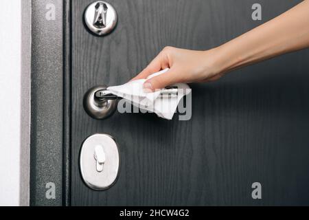 Pulizia delle maniglie nere delle portiere con un panno antisettico umido. Donna mano che usa un asciugamano per pulire la porta della stanza di casa link. Igienizzare le superfici in Foto Stock