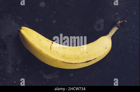 Frutta di banane gialle mature, mazzo di banane mature con macchie scure su sfondo scuro Foto Stock