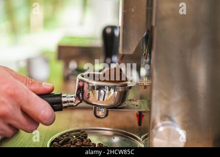 Mani del barista che tiene il portafiltro riempito di caffè macinato per prepararlo alla preparazione della macchina Foto Stock