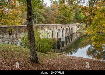 Vista ad angolo primo piano del ponte in pietra a sette archi che attraversa il lago Byrd nel parco statale circondato da vivaci alberi colorati in autunno Foto Stock