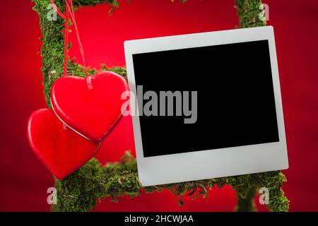 Due cuori e una cornice fotografica istantanea vuota su sfondo rosso Foto Stock