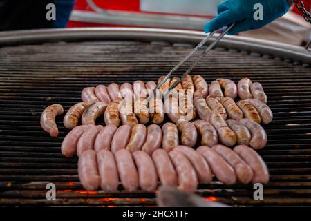 Chef grigliare salsicce di carne fresca su un grande grill rotondo - primo piano Foto Stock