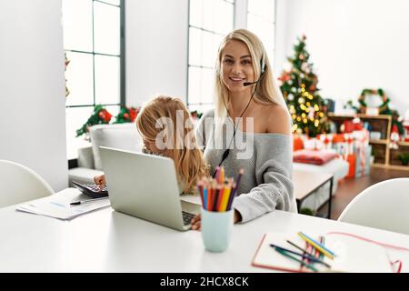 Madre di figlia caucasica che indossa la cuffia per agente del call center a casa, che guarda in piedi e sorridendo con un sorriso sicuro Foto Stock
