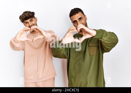 Giovane coppia gay in piedi su sfondo bianco isolato sorridendo in amore facendo il cuore simbolo forma con le mani. Concetto romantico. Foto Stock