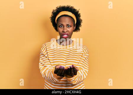 Giovane afroamericana che tiene le mani insieme, coccolato, dando concetto in faccia shock, guardando scettico e sarcastico, sorpreso con bocca aperta Foto Stock