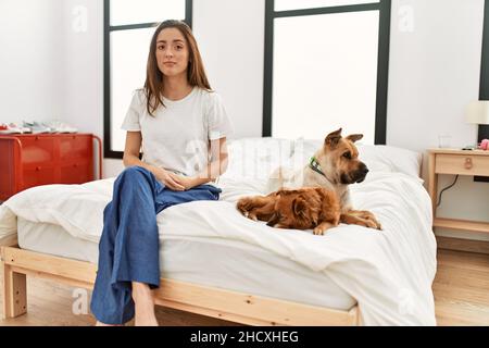 Giovane donna bruna seduta sul letto con due cani con espressione seria sul viso. Semplice e naturale guardare la macchina fotografica. Foto Stock