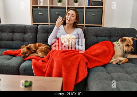Giovane donna ispanica che guarda il film seduto sul divano con i cani a casa Foto Stock