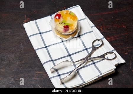 Torta con gelatina, kiwi, ciliegie e mango sul tavolo. Mini dessert yummy su sfondo di legno, primo piano. Foto Stock