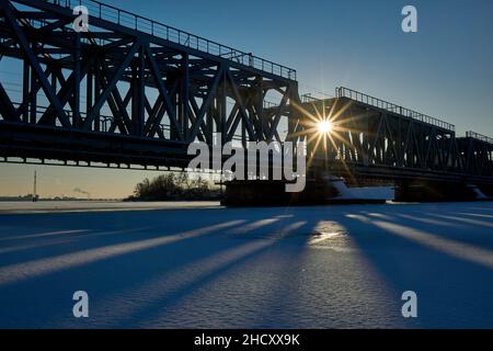 Voronezh, Russia. 27th Dic 2021. I raggi del sole attraverso il ponte ferroviario sopra il serbatoio di Voronezh durante il fine settimana di Capodanno.i previsori di Voronezh hanno dato una previsione per un lungo fine settimana di Capodanno. Questa volta, tranne l'inverno reale per durare tre giorni, la nevicata praticamente non si fermerà. I residenti della città trascorrono il fine settimana di Capodanno a piedi, facendo shopping, visitando cinema e parchi. Molte istituzioni operano con restrizioni antivirali. All'ingresso, le persone devono avere codici Quar che confermano la vaccinazione o la presenza di anticorpi. Altri stabilimenti sono Foto Stock