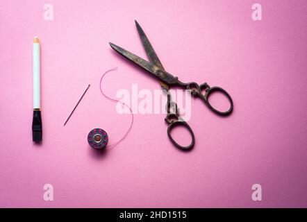 rocchetto o rocchetto di filo e forbici con ago per cucire su sfondo rosa , hobby e passatempi , immagine minimalista . Foto Stock