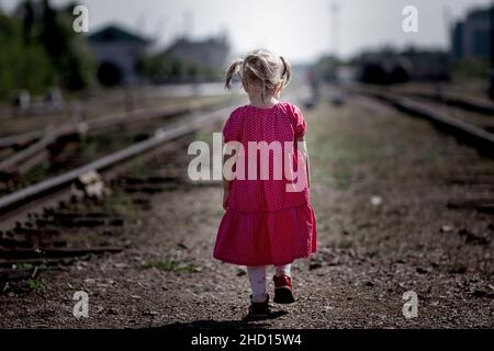 Dietro di bambino caucasico bambino bambina che va da sola sulla ferrovia. Concetto bambini abbandonati Foto Stock